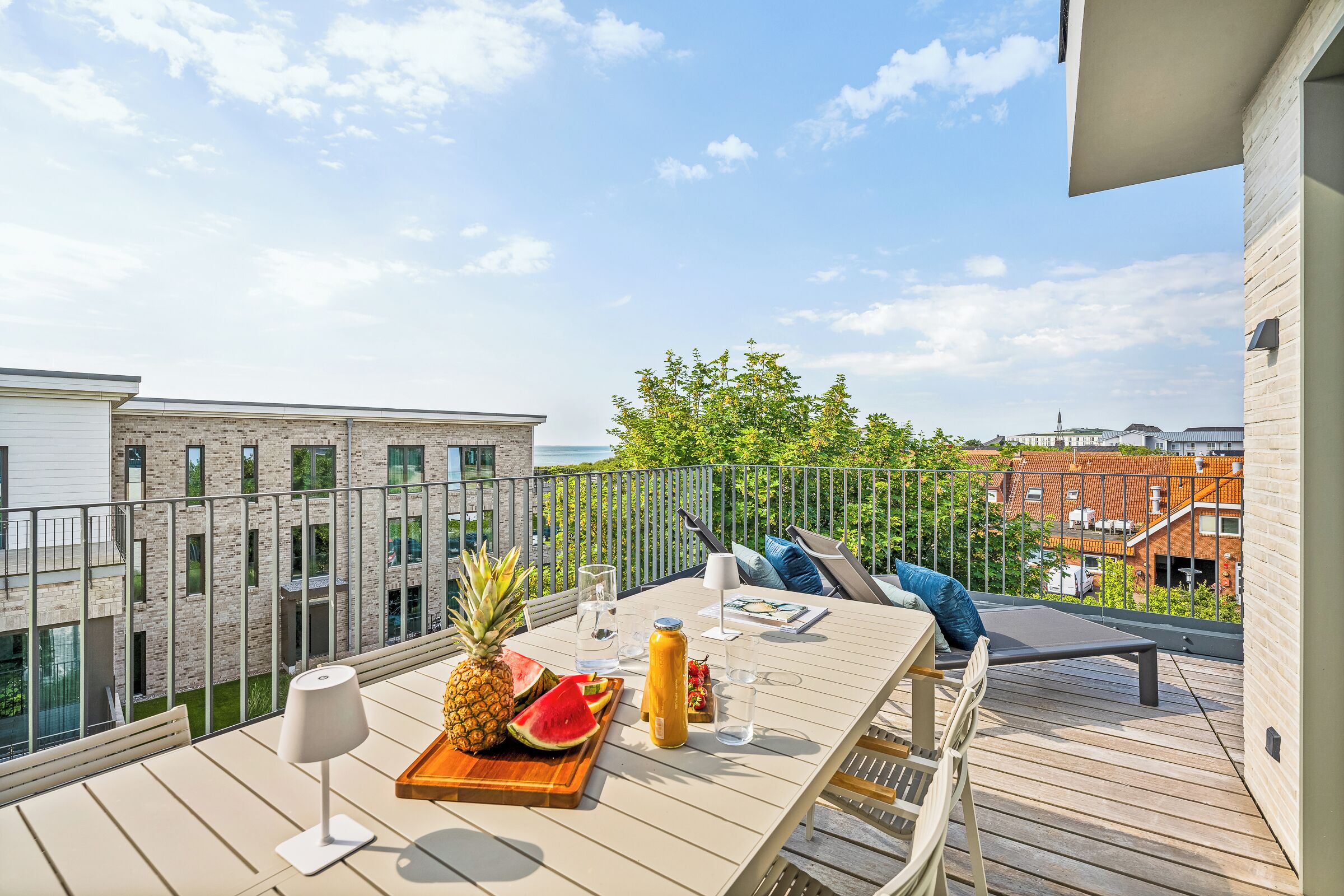 A balcony with a table set for two, a chair, a railing, and a view of buildings and trees.