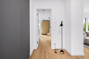 Ein modernes Interieur mit Holzboden, einer schwarzen Stehlampe und Blick in einen Raum mit einer Holztür und einem Sessel.