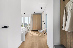 A modern interior with a wooden floor, a white sofa, a wooden panel wall, and a view through a large window. - Arrival amid the sea, light, and open landscape (List auf Sylt)