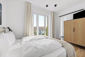 Ein modernes Schlafzimmer mit einem gro ßen Bett, einem Kleiderschrank und Blick ins Freie.
