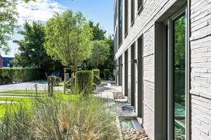Ein modernes Gebäude mit Ziegelaußenwand, großen Fenstern und einem gepflegten Garten mit Hecken und Bäumen.