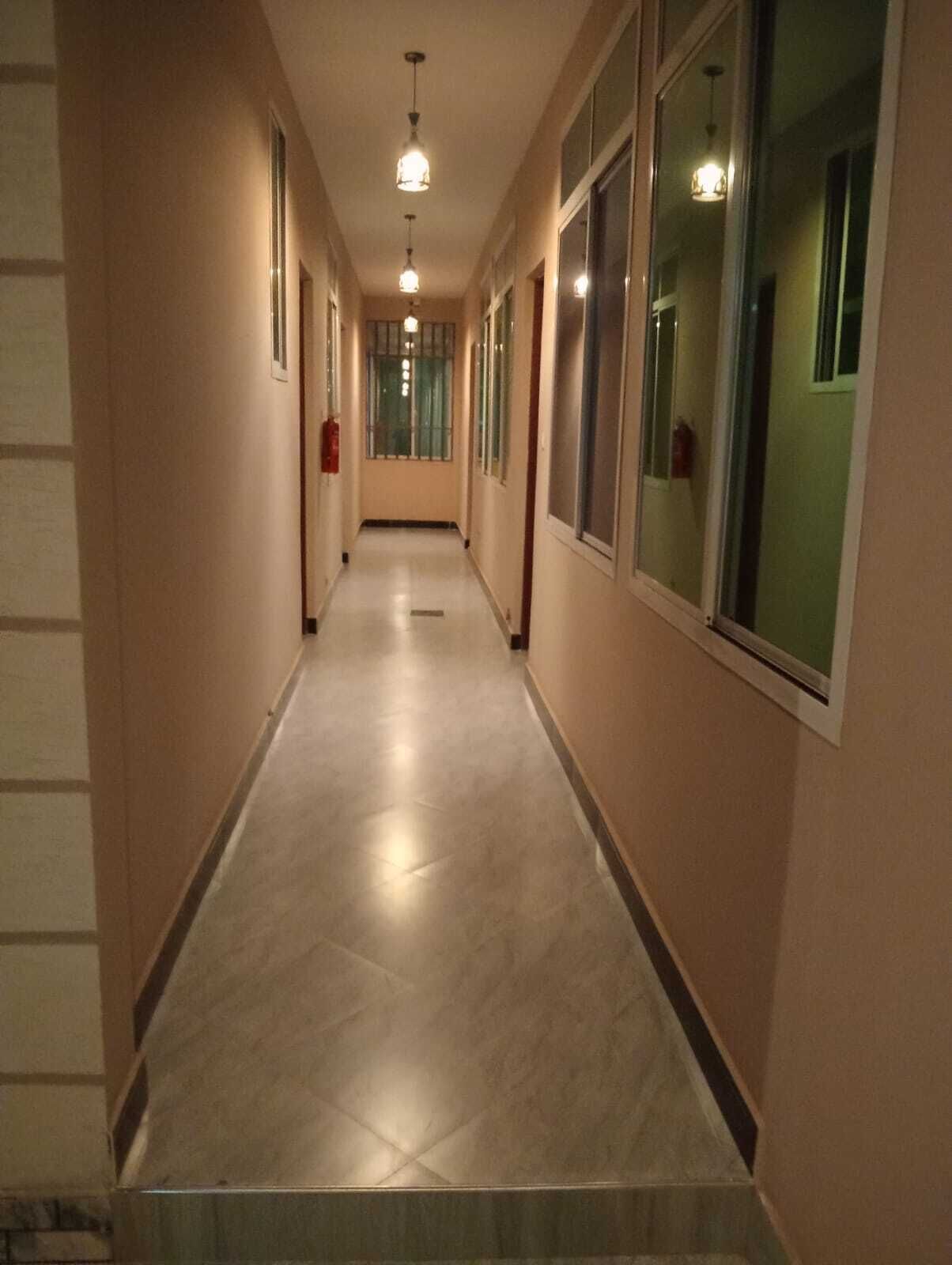 A corridor with a tiled floor, large windows, and hanging lights.