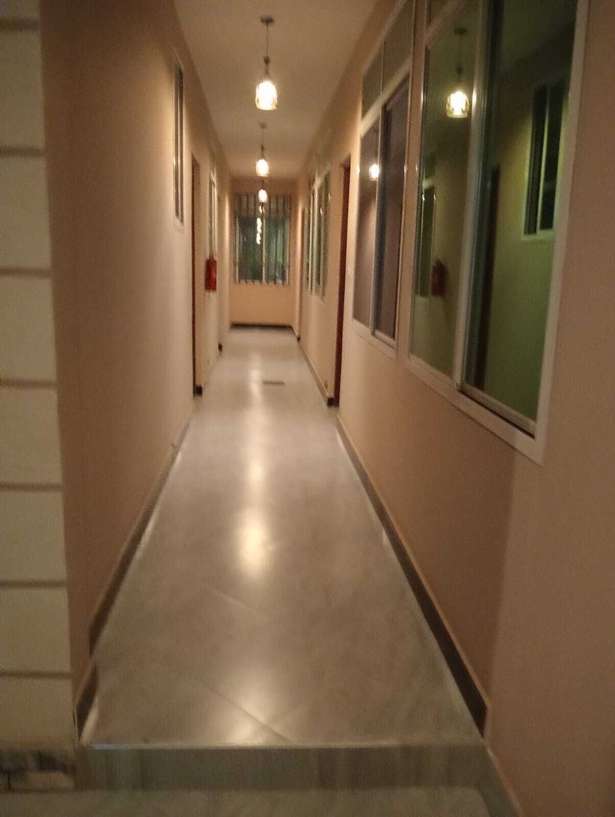 En lang, smal gang med lyse gulvbrædder, store vinduer på den ene side og hængende lamper.