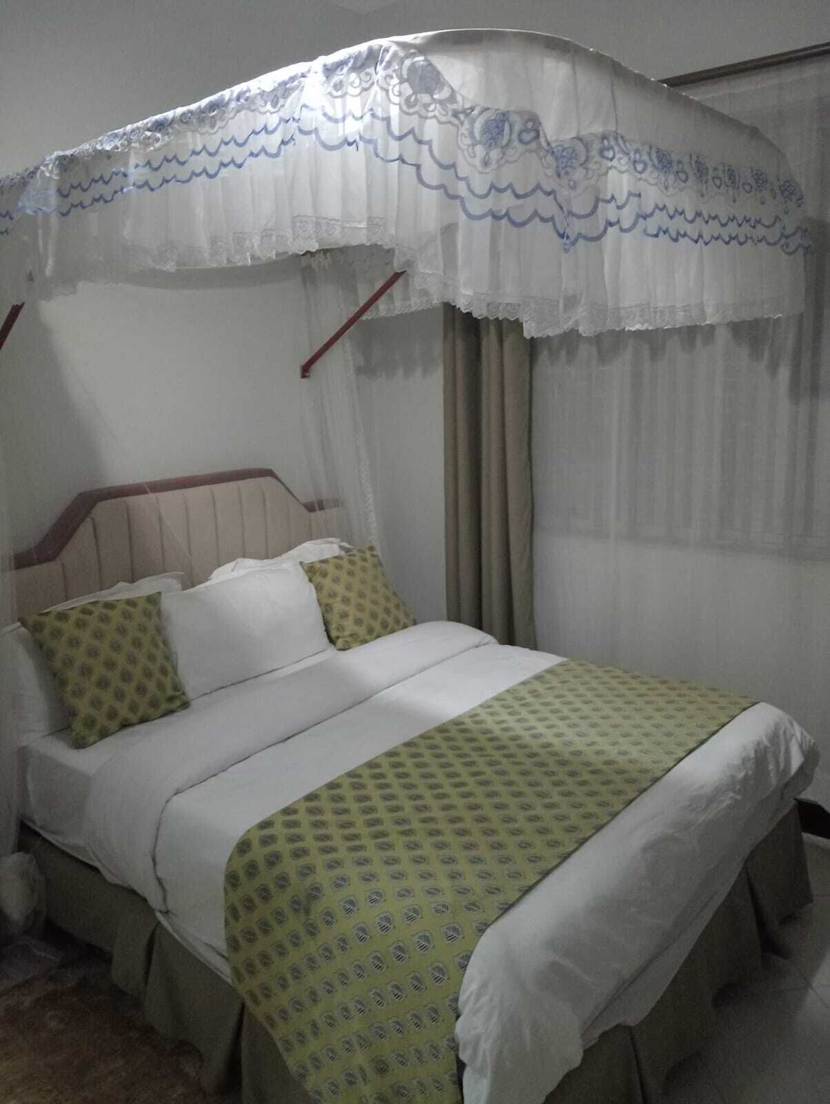 A single bed with a canopy, two pillows, and a patterned bedspread.