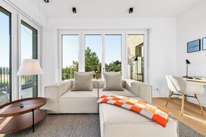 A modern living room with a sofa, a small table, a desk, and large windows. - Arriving between the sea, the light, and the open landscape (List auf Sylt)