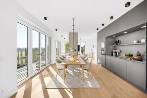 A modern kitchen with grey cabinets, a wooden dining table, and a large window overlooking a balcony. - Arriving between the sea, the light, and the open landscape (List auf Sylt)