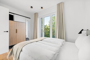 A modern bedroom with a large bed, a wardrobe, and a window with curtains. - Arriving between the sea, the light, and the open landscape (List auf Sylt)