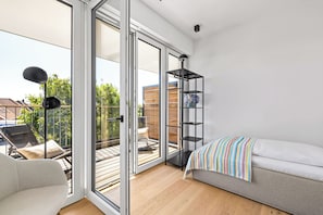 A modern room with a sofa, a bookshelf, and a balcony with outdoor furniture. - Arriving between the sea, the light, and the open landscape (List auf Sylt)