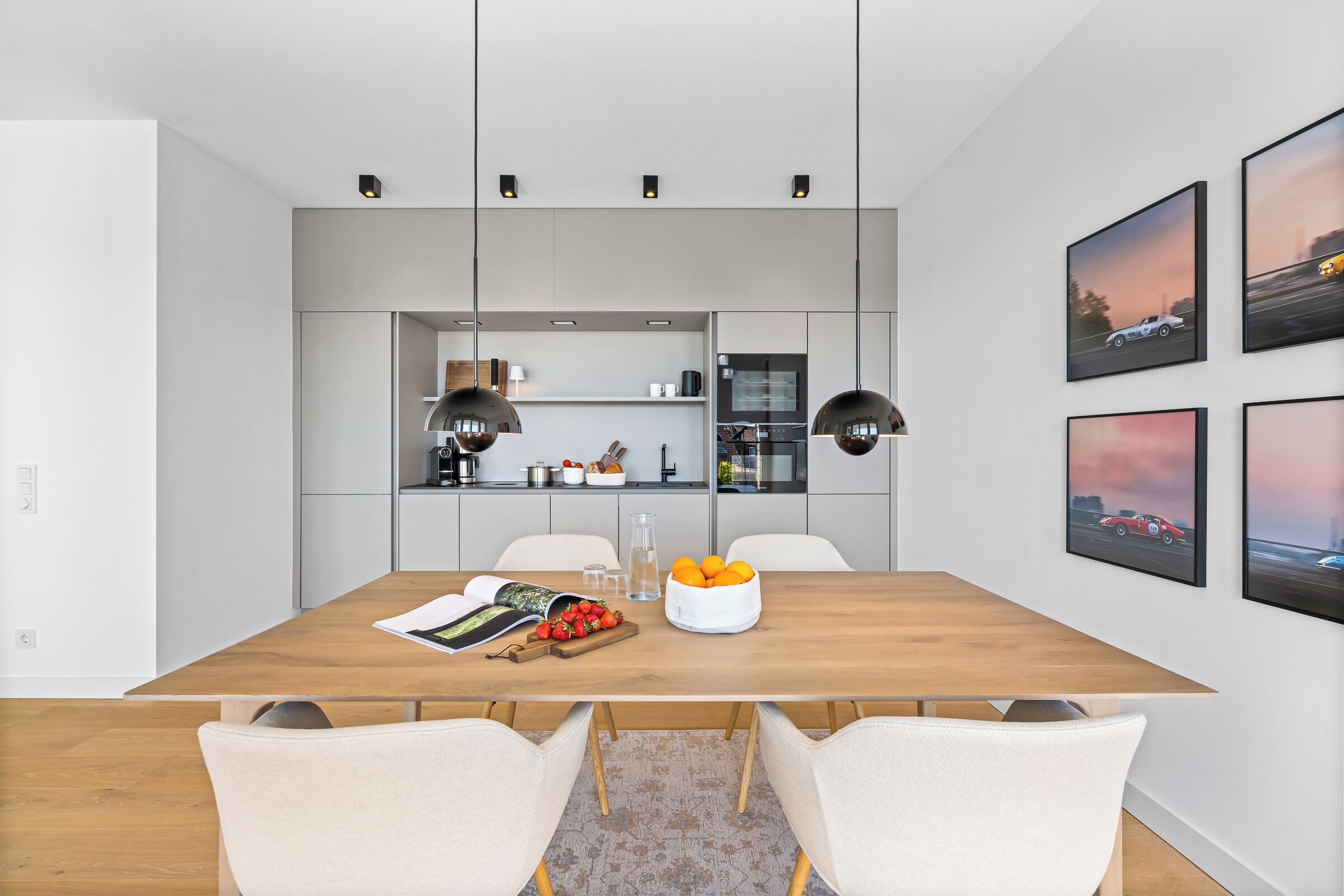 Un espace repas moderne avec une table en bois, des chaises blanches, des luminaires suspendus et des tableaux encadrés accrochés au mur.