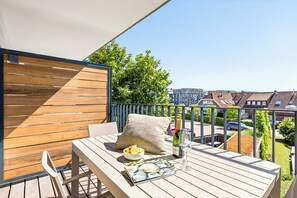 A balcony with a wooden table, a cushion, a bowl of lemons, a bottle of champagne, and a glass. - Arriving between the sea, the light, and the open landscape (List auf Sylt)