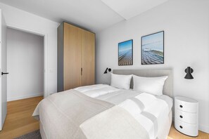 A modern bedroom with a bed, a wardrobe, a bedside table, and two wall-mounted pictures. - Set against the backdrop of the sea, the light, and the open landscape (List auf Sylt)