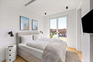 A modern bedroom with a large bed, a TV, and a view of the outside. - Arriving between the sea, the light, and the open landscape (List auf Sylt)