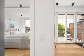 A modern bedroom with a bed, a bedside table, and a view of a balcony with outdoor furniture. - Arriving between the sea, the light, and the open landscape (List auf Sylt)