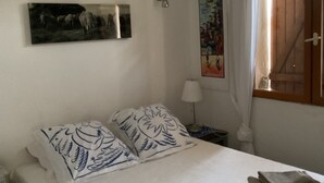 Et soveværelse med en seng, et natbord, en lampe, et vindue med gardiner og et billede på væggen.