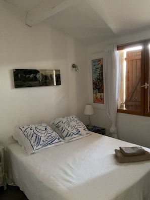 Ein Schlafzimmer mit einem Bett, einem Nachttisch, einer Lampe, einem Fenster mit Vorhängen und einem Bild an der Wand.