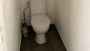 Et lille badeværelse med toilet, en hylde over toilettet og en moppe på gulvet.
