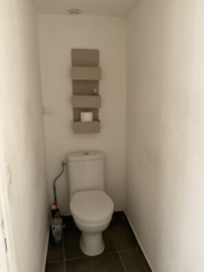 Ein kleines Badezimmer mit Toilette, einem Regal darüber und einem Wischmopp auf dem Boden.