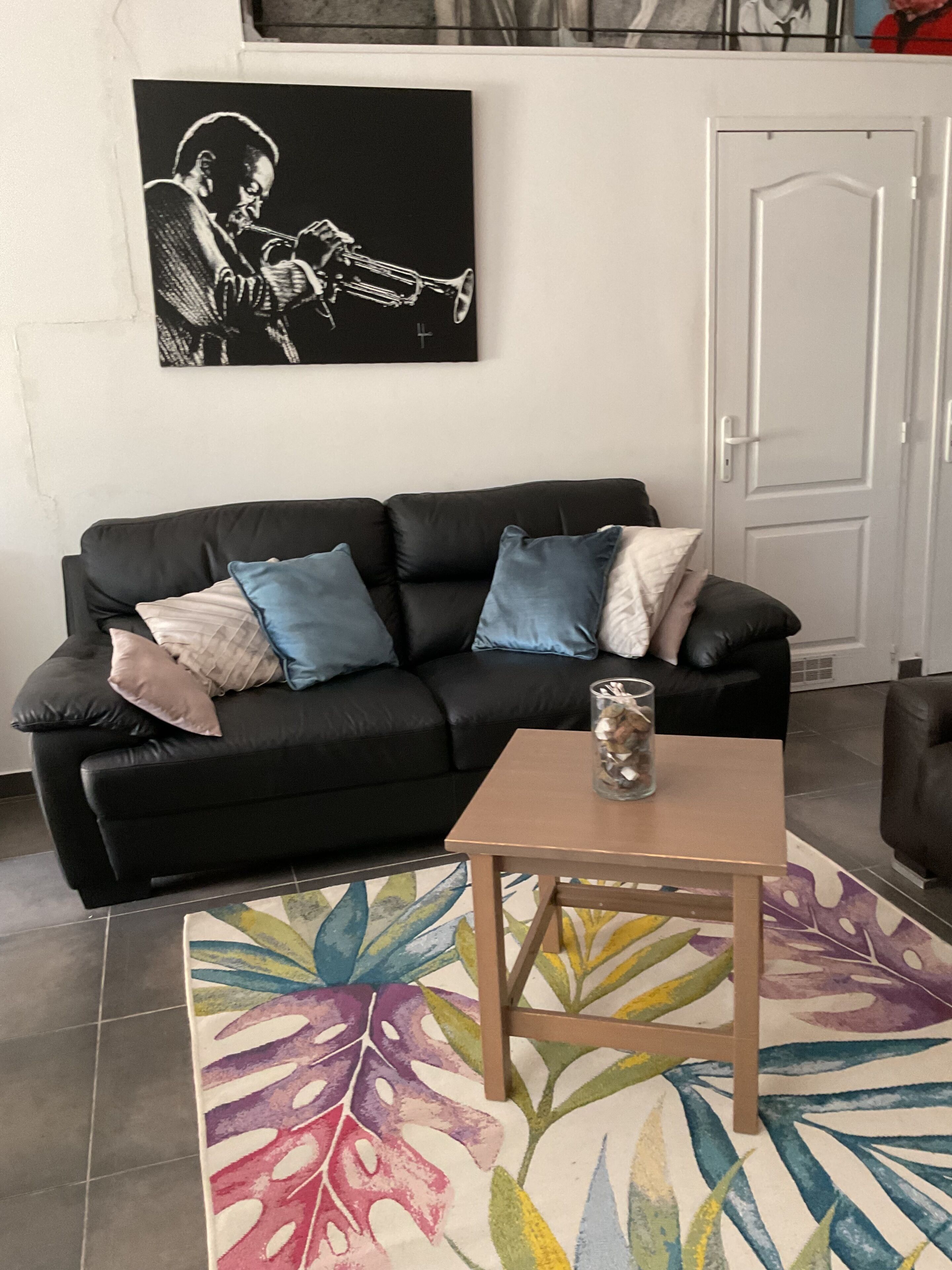 A living room with a black sofa, colorful rug, and a small wooden table.