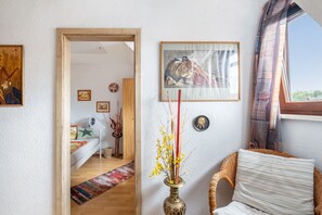 Una habitación con una cama, una silla, un florero con flores y un cuadro en la pared.