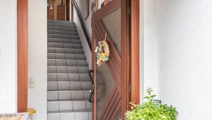 Eine Treppe führt zu einer Holztür, verziert mit einem Kranz, einem Blumentopf und einer Wandleuchte.