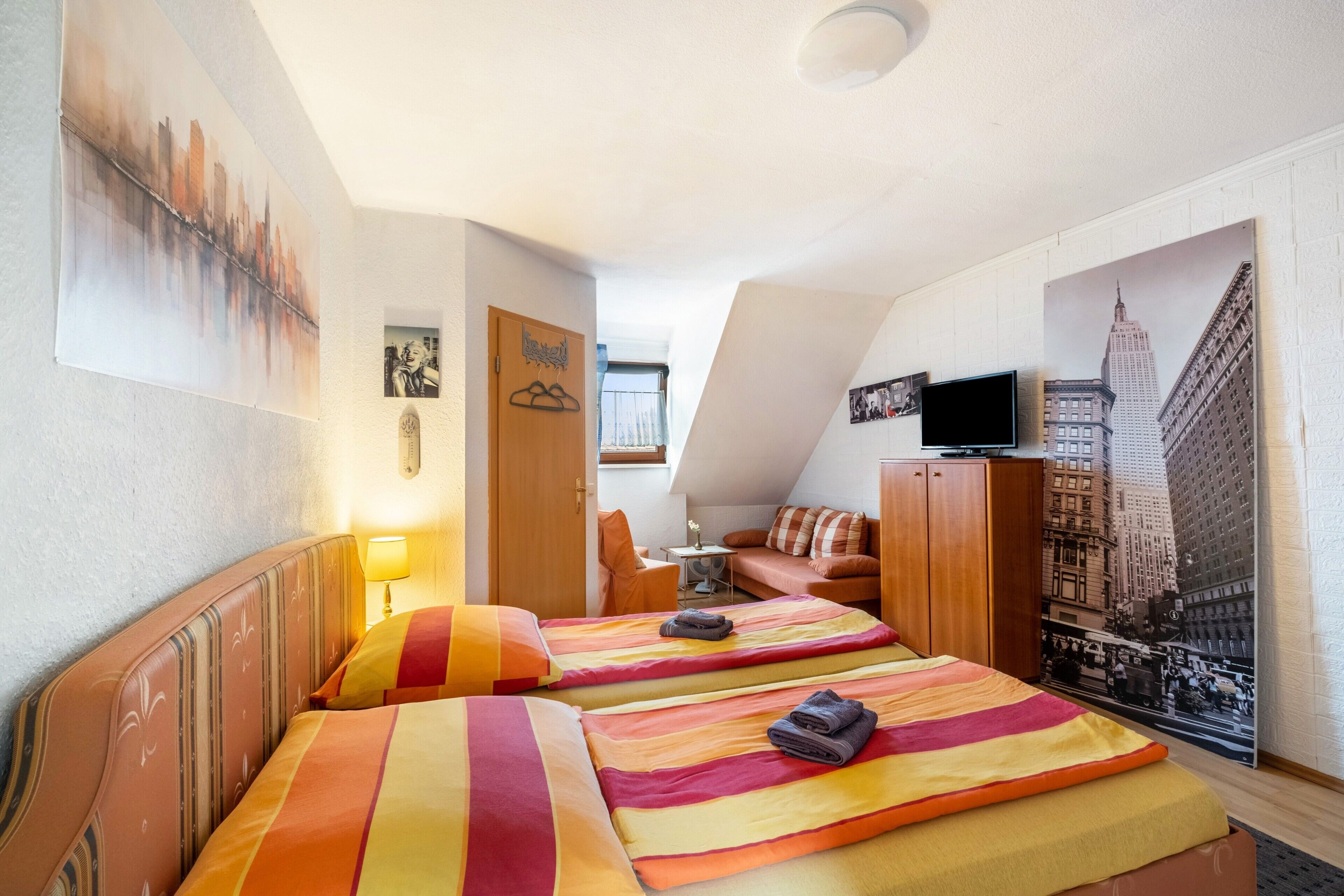 Une chambre d’hôtel avec deux lits, une télévision et une décoration murale représentant un paysage urbain.