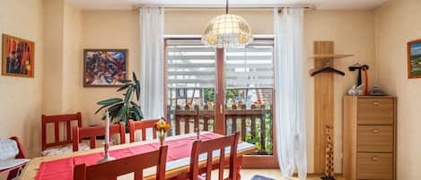 A dining area with a table set for four, wooden chairs, a hanging light fixture, and a view of the street through a window with blinds.