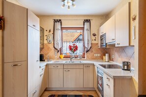 Eine moderne Küche mit hellen Holzschränken, einem eingebauten Ofen und einem Fenster mit Vorhängen.