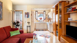 Ein kompakter Wohnraum mit Küchenzeile, einem roten Sofa, einem Flachbildfernseher und einem Bücherregal.