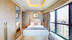 Ein Hotelzimmer mit einem großen Bett, einem Nachttisch, einem Schrank und einem Fenster mit Blick auf die Stadt.
