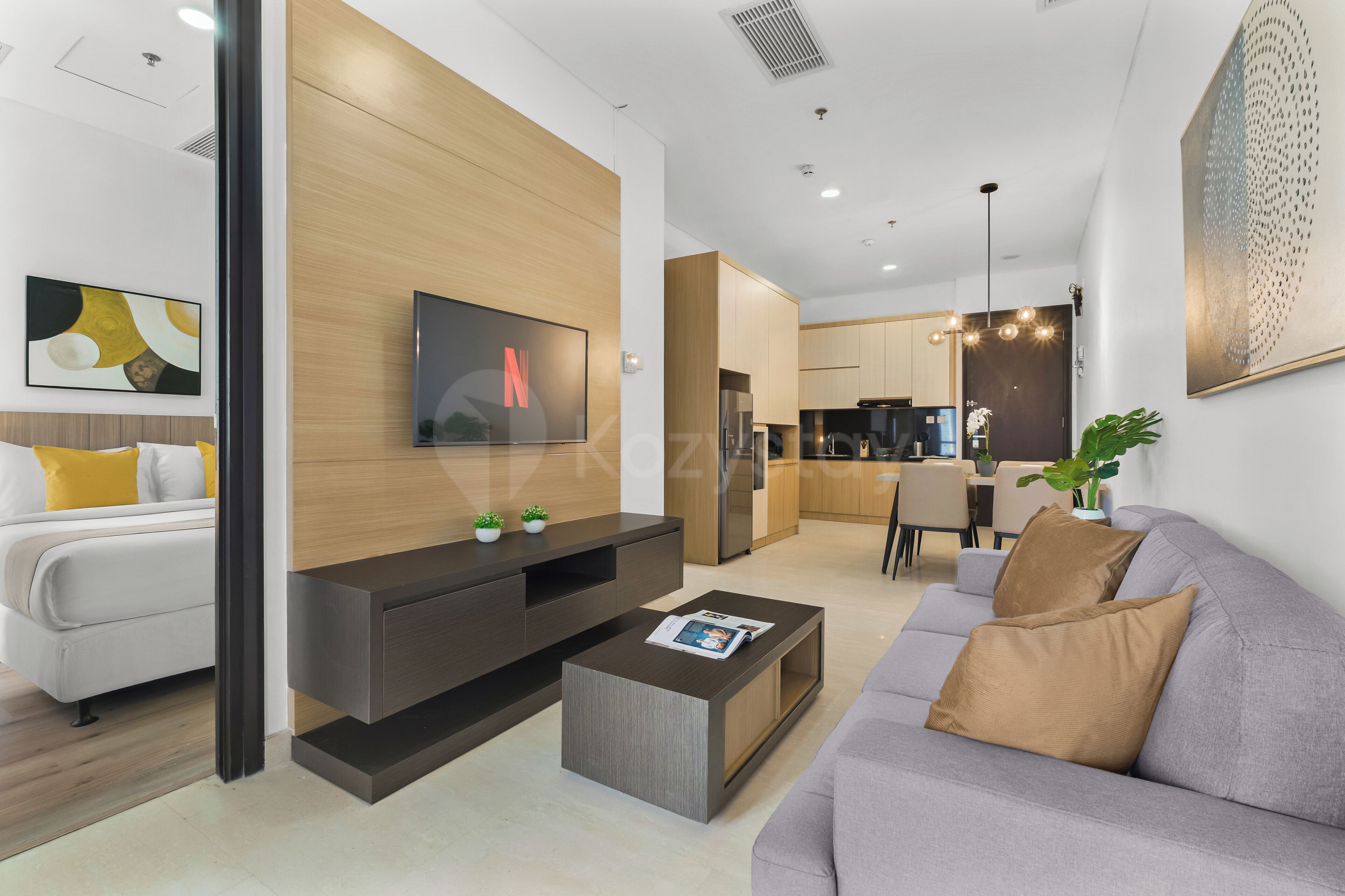 A modern living room with a flat-screen TV, a sofa, a coffee table, and a dining area in the background.