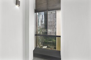 Ein Zimmer mit Fenster, Wandleuchte und Blick auf Gebäude und Grünflächen.