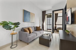 Ein modernes Wohnzimmer mit grauem Sofa, einem Couchtisch, einem Fernseher und einer Pflanze.