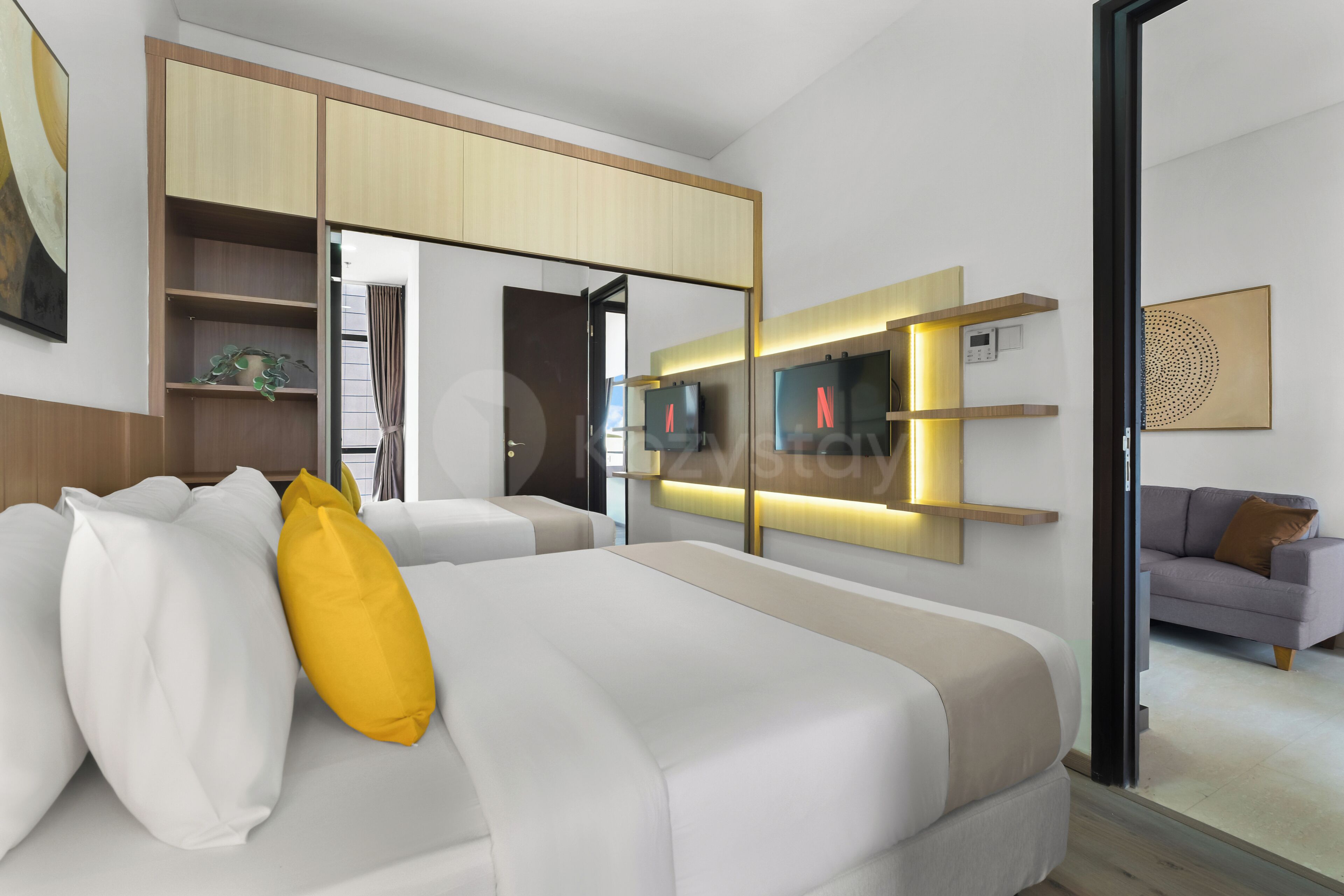 A modern hotel room with a bed, a sofa, a TV, and a wall-mounted shelf.