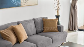 A modern living room with a grey sofa, two cushions, a magazine on a coffee table, and a vase with branches. - Kaeva by Kozystay - Sudirman (Central Jakarta)