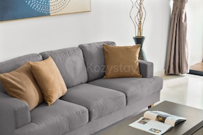 Ein modernes Wohnzimmer mit einem grauen Sofa, zwei Kissen, einer Zeitschrift auf einem Couchtisch und einer Vase mit Zweigen.