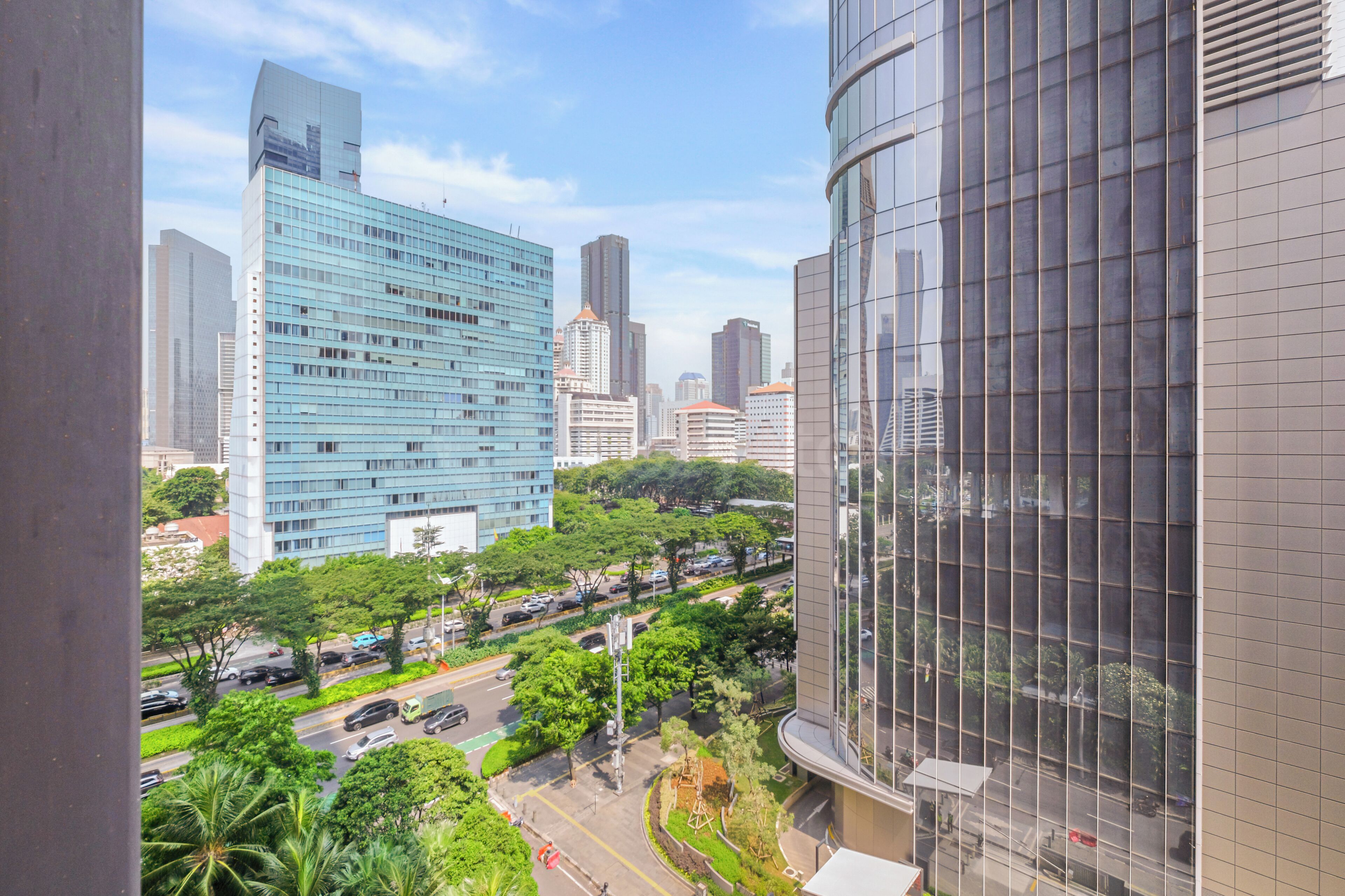A cityscape with modern buildings, a road with cars, and greenery.