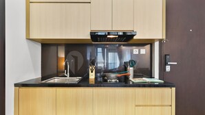 A modern kitchen with a black countertop, wooden cabinets, and a built-in oven. - Kaeva by Kozystay - Sudirman (Central Jakarta)