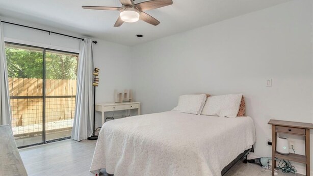 Une chambre à coucher avec un lit, un ventilateur de plafond, une table de chevet et une fenêtre avec des rideaux.