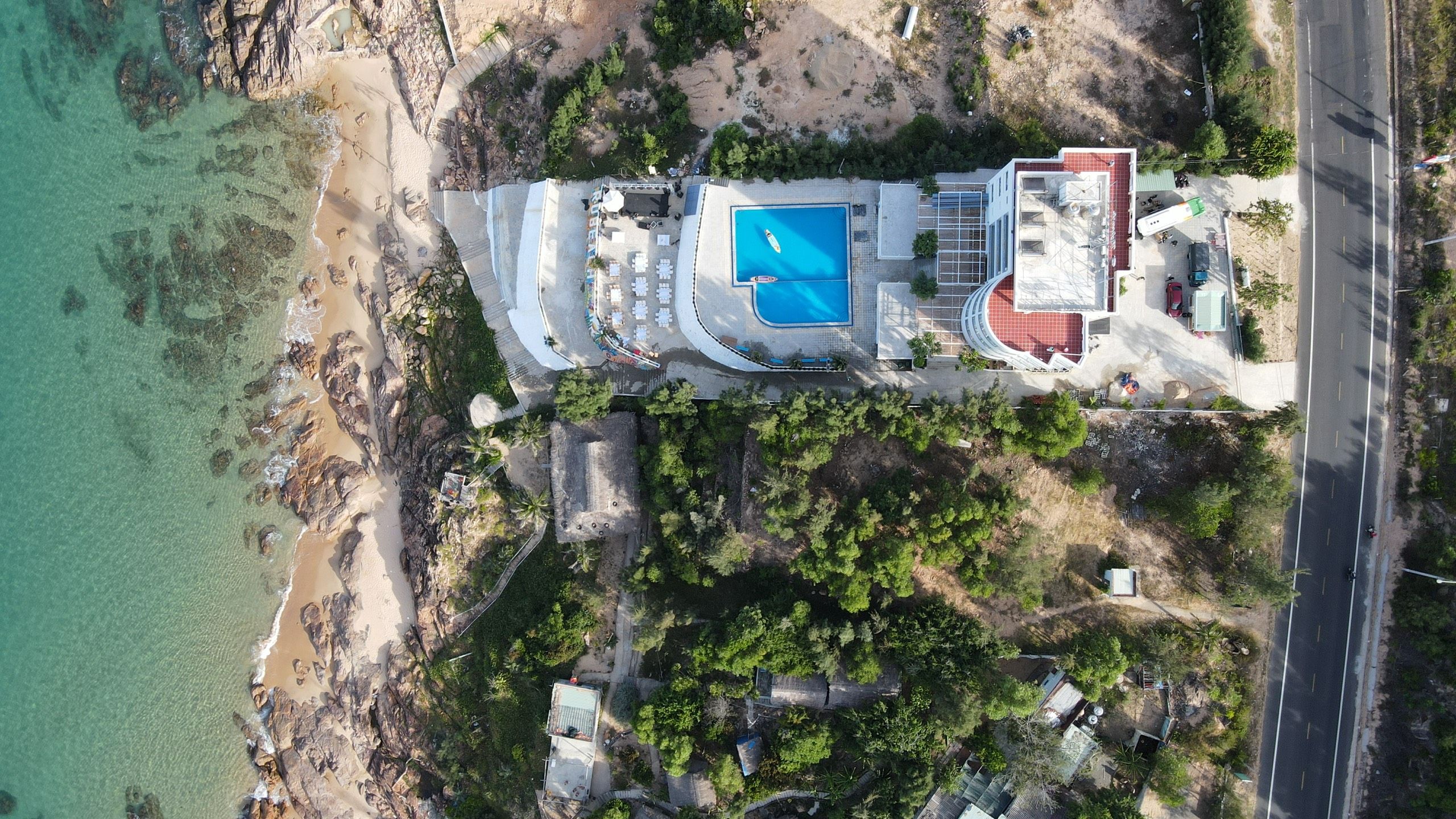 An aerial view of a resort with a swimming pool, beach access, and lush vegetation.