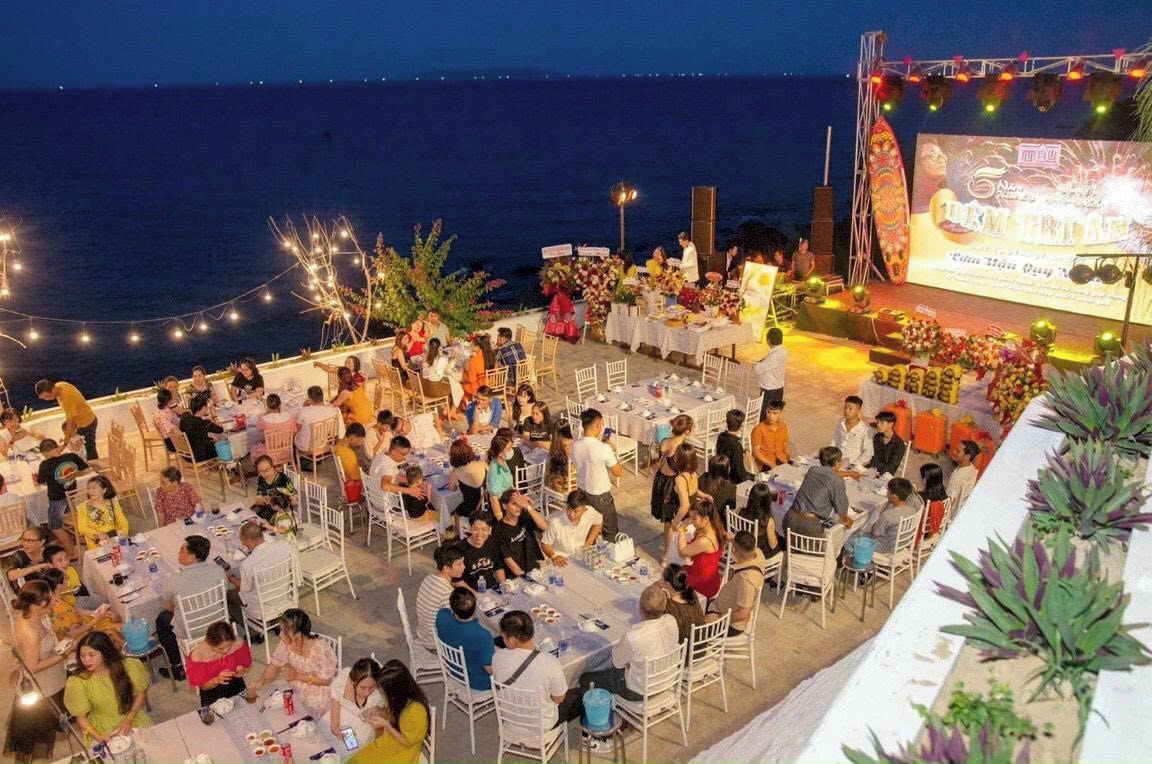 An outdoor dining area with tables and chairs arranged for guests, overlooking a body of water.