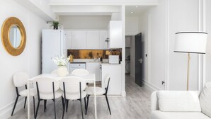 Een moderne keuken met witte kastjes, een eethoek met een witte tafel en stoelen, en een zithoek met een bank.