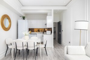 A modern kitchen with white cabinets, a dining area with a white table and chairs, and a living area with a sofa. - Maida Vale Apartments (London)