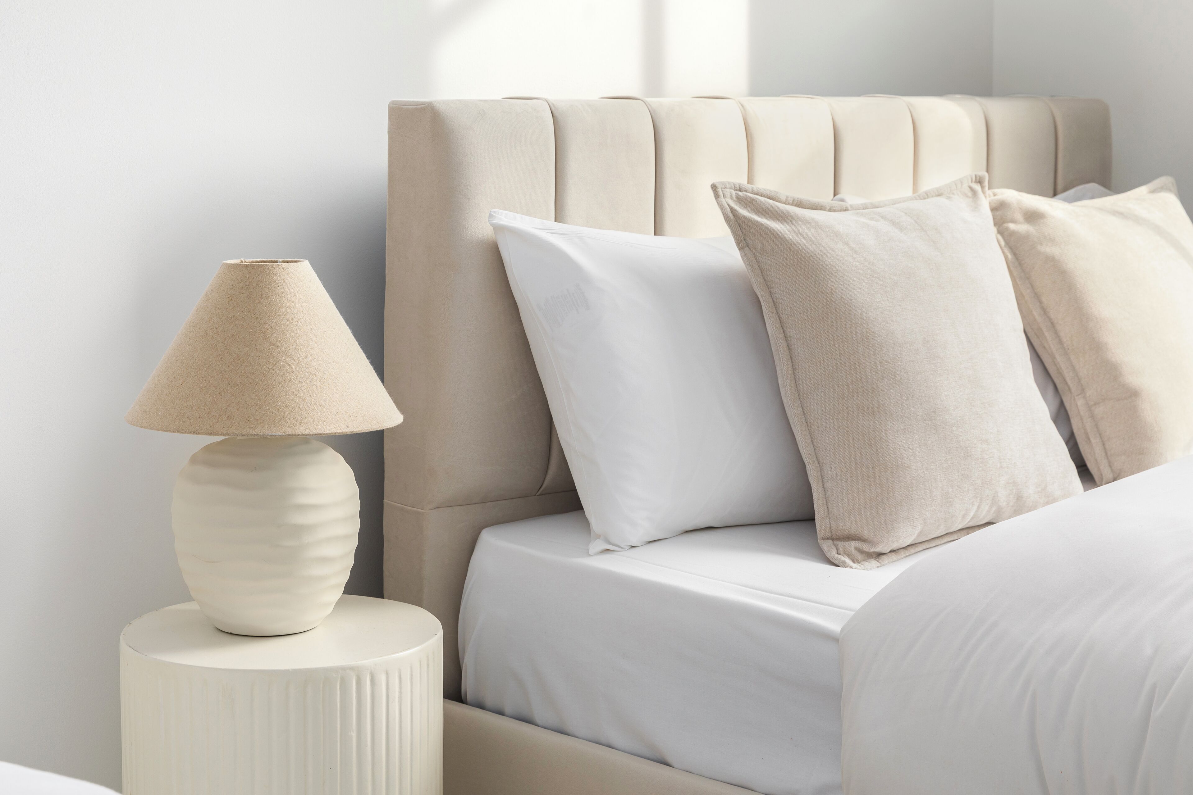 Cama com cabeceira, almofadas e abajur em uma mesa de cabeceira.