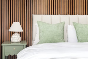 A neatly made bed with white bedding, a green nightstand with a lamp, and two green pillows. - Maida Vale Apartments (London)