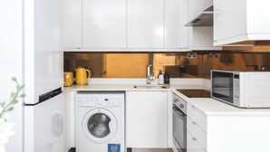 Een kleine keuken met witte kastjes, een wasmachine, een magnetron en een spoelbak.