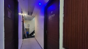 A narrow hallway with closed wooden doors, a visible staircase, and a blue-lit ceiling.