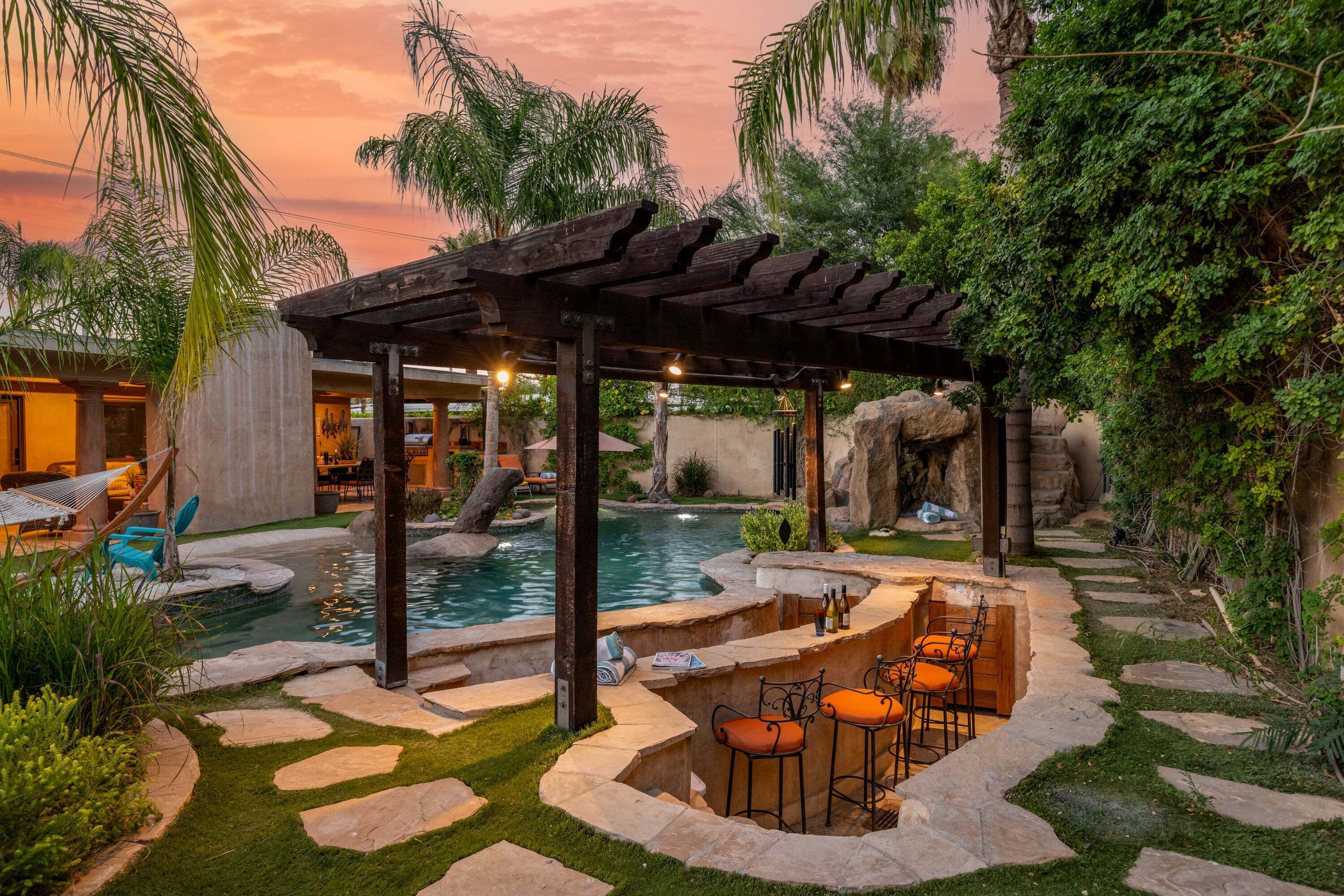 A pool area with a pergola, seating, and a natural rock backdrop.