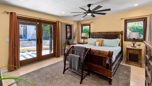A bedroom with a bed, a ceiling fan, a nightstand, a lamp, and a view through the glass doors. - Desert Dunes | Lazy River & Water Slide | Swim-Up Bar | Dual Casitas | Sleeps 8 (Palm Springs)