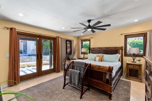 Ein Schlafzimmer mit einem Bett, Deckenventilator, Nachttisch, Lampe und Blick durch die Glastüren.