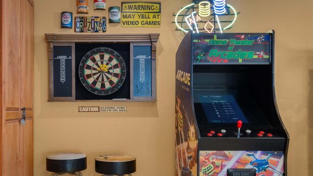 A room with a dartboard, a warning sign about video games, and an arcade machine. - Desert Dunes | Lazy River & Water Slide | Swim-Up Bar | Dual Casitas | Sleeps 8 (Palm Springs)